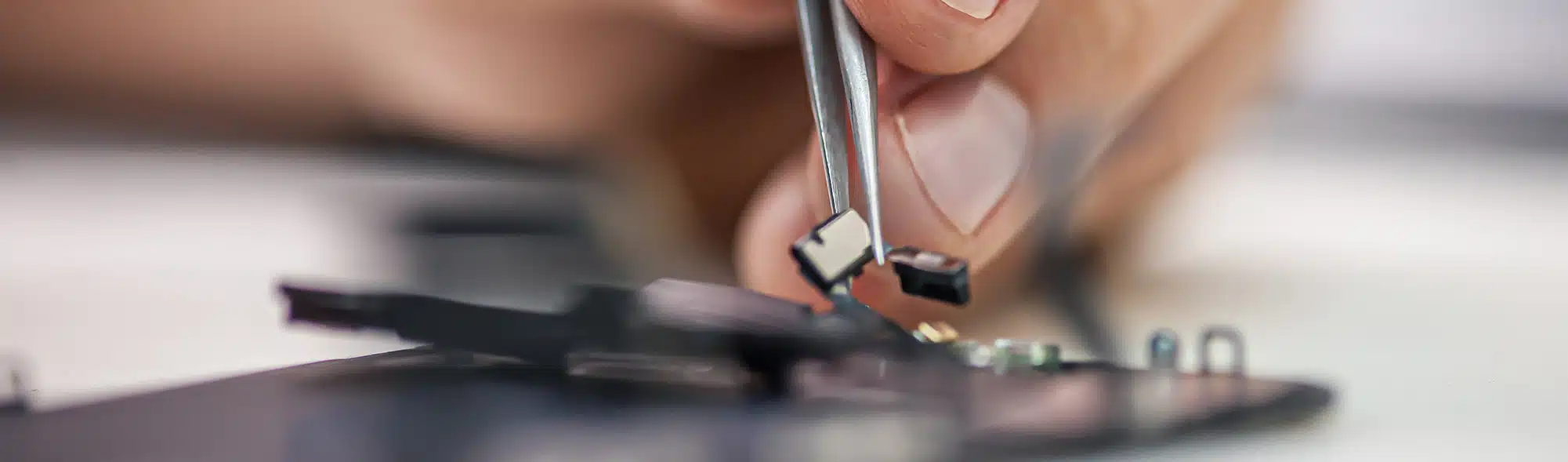 Technician repairs smartphone, uses tweezers as tool in electronics workshop
