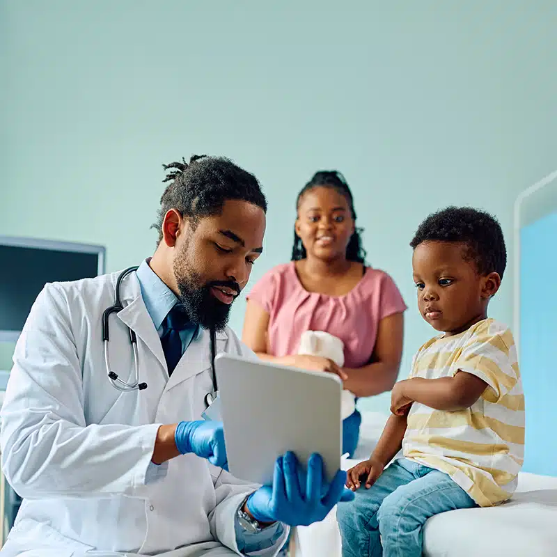 Black kid and his pediatrician using digital tablet at doctor's office.
